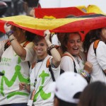 People shelter themselves from the rain under Spanish flags as they wait for the arrival of Pope Benedict XVI in Madrid